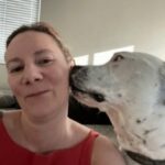 female wearing red tank top getting kisses on her cheek from a large white dog