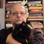 male with glasses and mustache holding a black cat